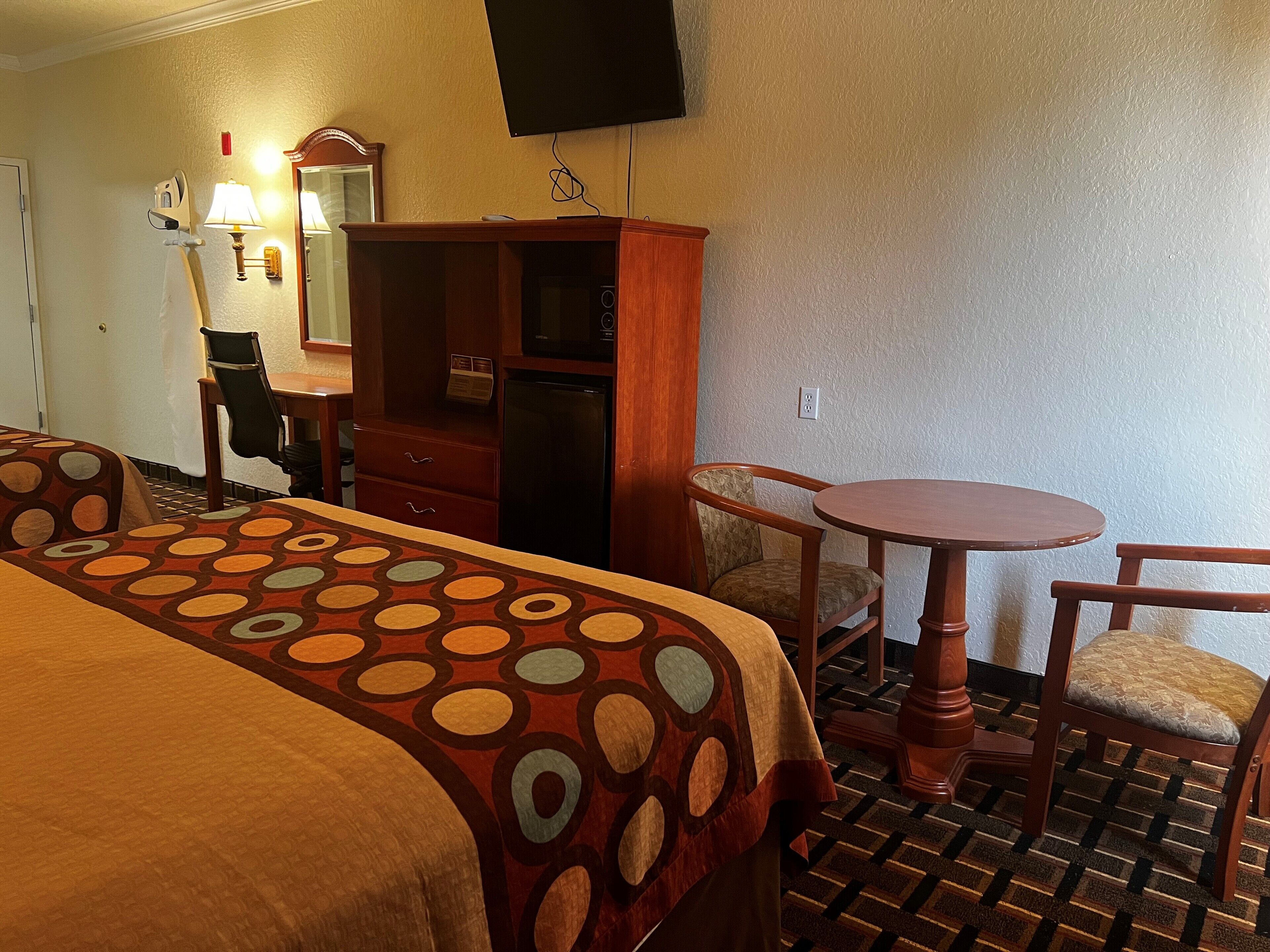 A hotel room with two beds, a desk, a chair, a small table, a microwave, and a television.