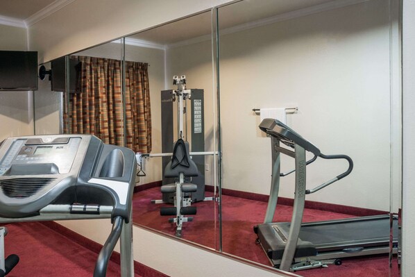 Un gimnasio con cinta de correr, máquina de pesas y un espejo grande.