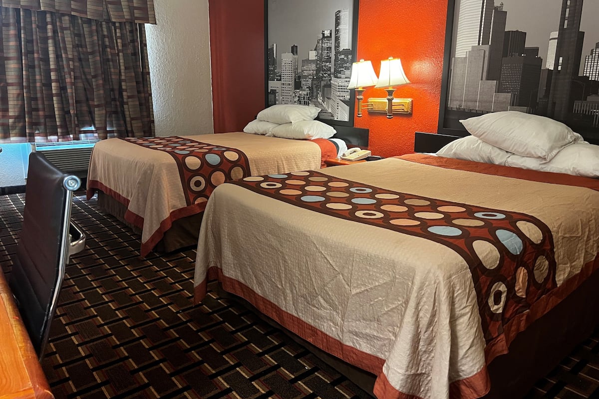 Een hotelkamer met twee bedden, een stadsmuur als decoratie, een bureau en een televisie.