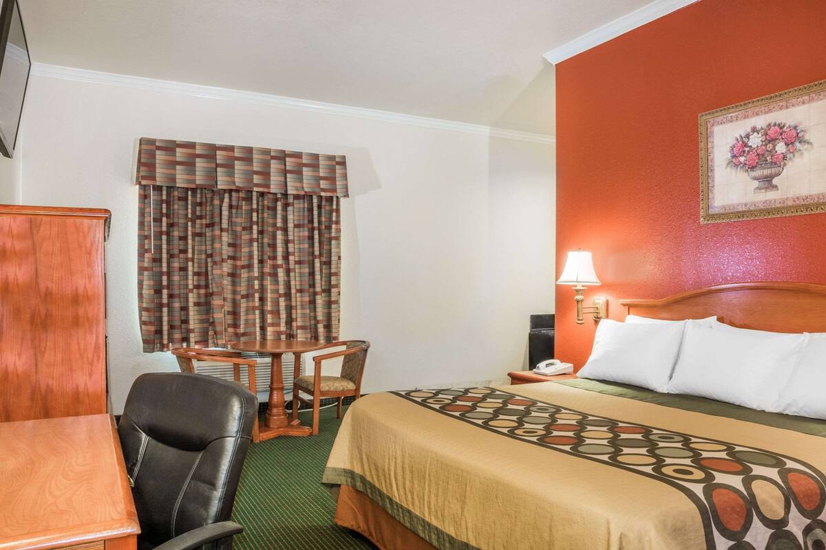 Een hotelkamer met een bed, een bureau, een stoel, een lamp en een schilderij aan de muur.