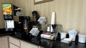 Un espace d’accueil d’hôtel équipé d’une machine à café, d’un distributeur de jus et de divers accessoires, tels que des tasses, des serviettes et des couverts.