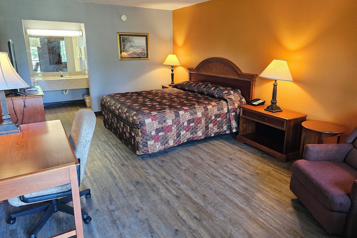 A hotel room with a bed, two bedside lamps, a desk with a chair, a small table, and a mirror.
