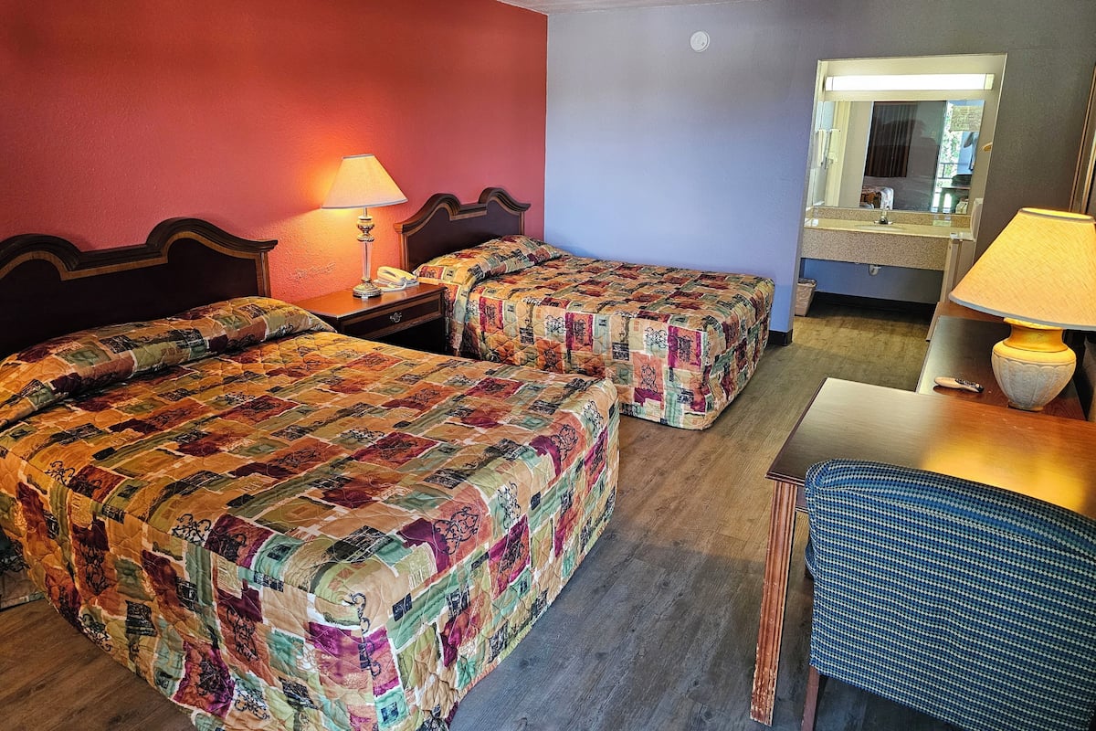 A hotel room with two beds, a desk, a chair, a lamp, and a mirror.