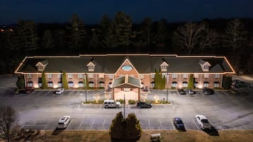 Un hotel grande con entrada central, varios espacios de estacionamiento y fachada bien iluminada.