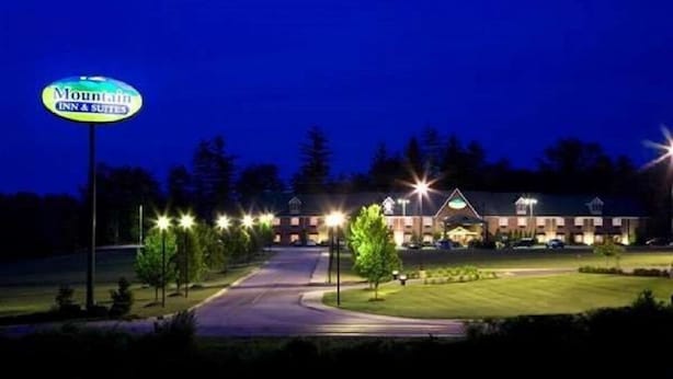 Edificio del Mountain Inn & Suites de noche, con señalización iluminada, un camino bien iluminado y un estacionamiento.