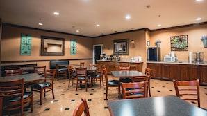 Un restaurante con varias mesas y sillas, una zona de cocina y decoración en las paredes.