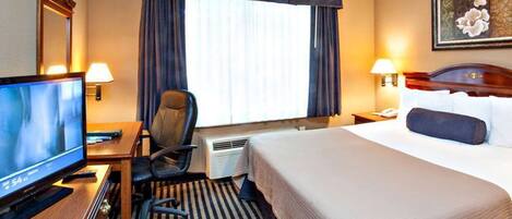 Habitación de hotel con cama, escritorio con televisor, silla, lámpara de escritorio, mesita de noche con teléfono y ventana con cortinas.
