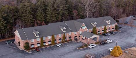 A multi-story hotel with a parking lot and a view of the surrounding forest.