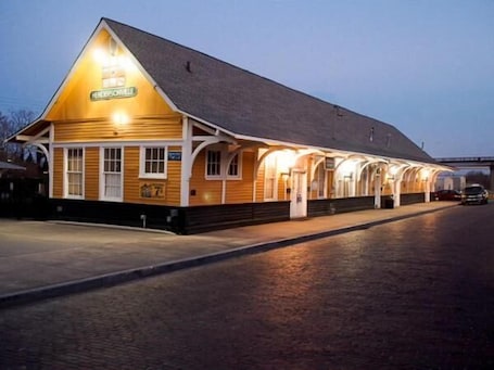 A long, single-story building with a sloped roof, a sign reading "Hendersonville," and a covered walkway with multiple windows.