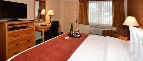 Ein Hotelzimmer mit einem Bett, einem Schreibtisch mit Computer, einem Fernseher und einem Fenster mit Vorhängen.