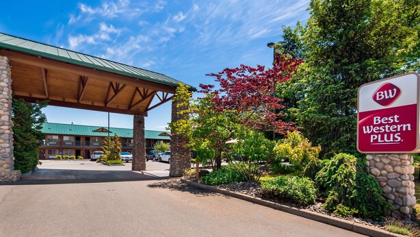 A Best Western Plus hotel with a covered parking area, stone pillars, and a variety of trees. - Best Western Plus Hartford Lodge (Sutherlin)