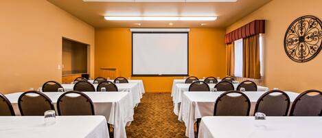 A conference room with tables and chairs, a projector screen, and a patterned carpet.