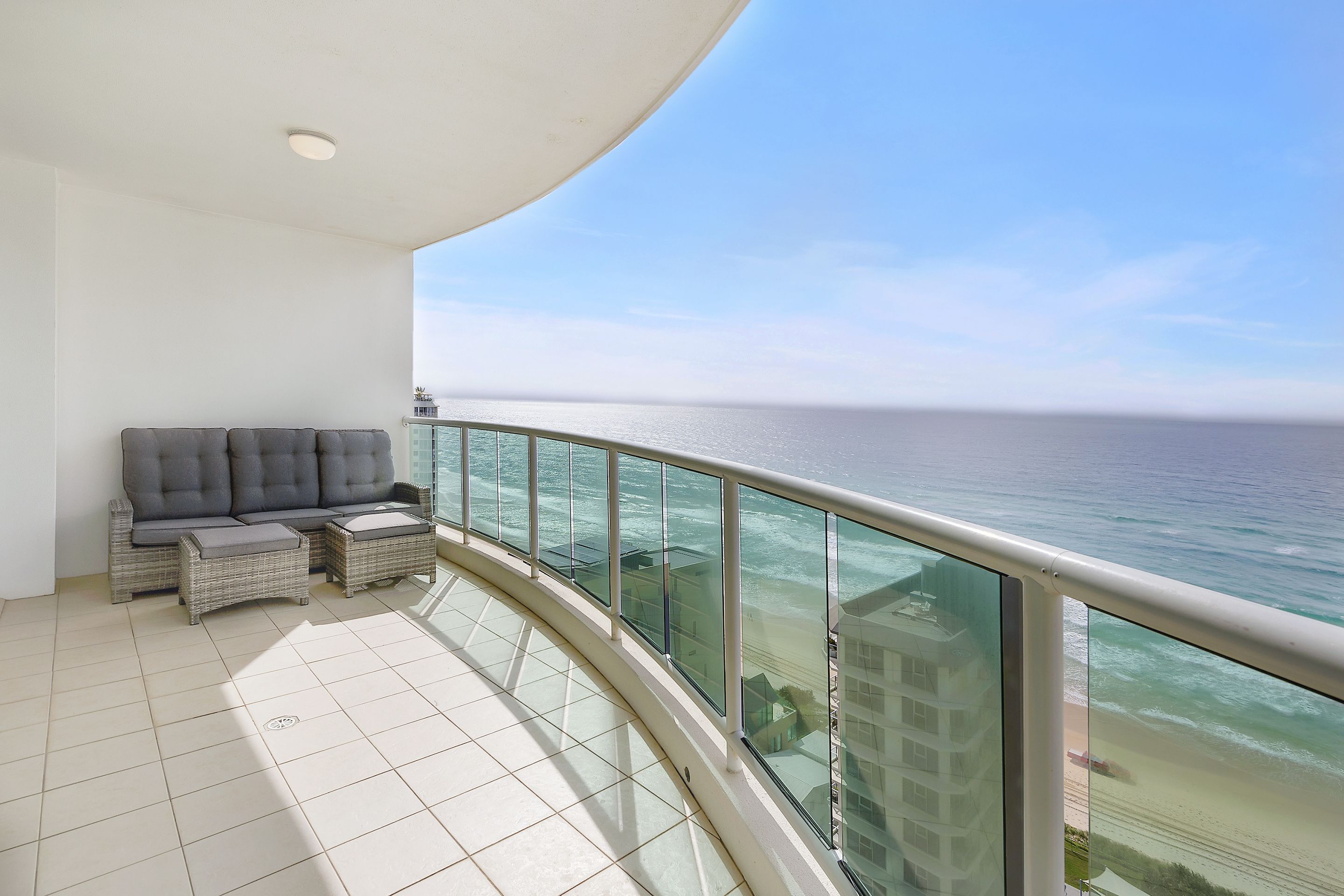 Un balcon avec vue sur l’océan, un canapé gris et une rambarde en verre.