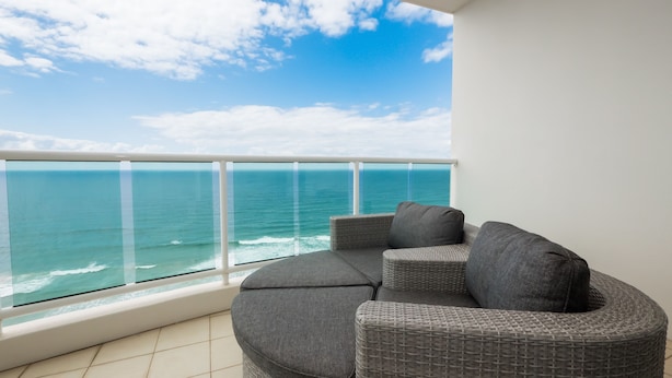 Un balcon avec vue sur l’océan, un canapé gris avec des coussins et une balustrade blanche.