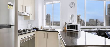 Una cocina moderna con electrodomésticos de acero inoxidable, una encimera negra y vistas de la ciudad a través de amplias ventanas.