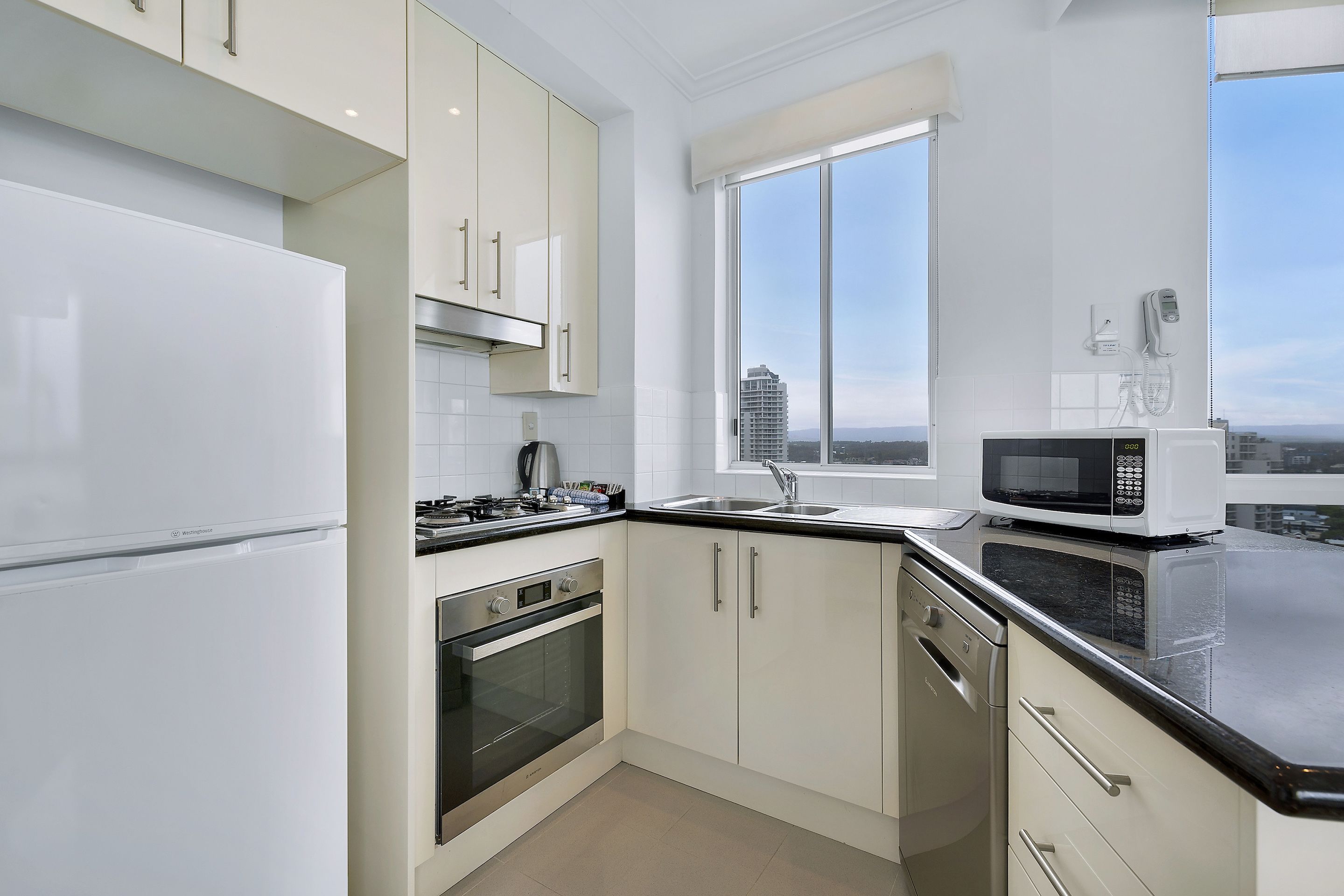 A modern kitchen with white cabinets, stainless steel appliances, and a large window offering a city view.