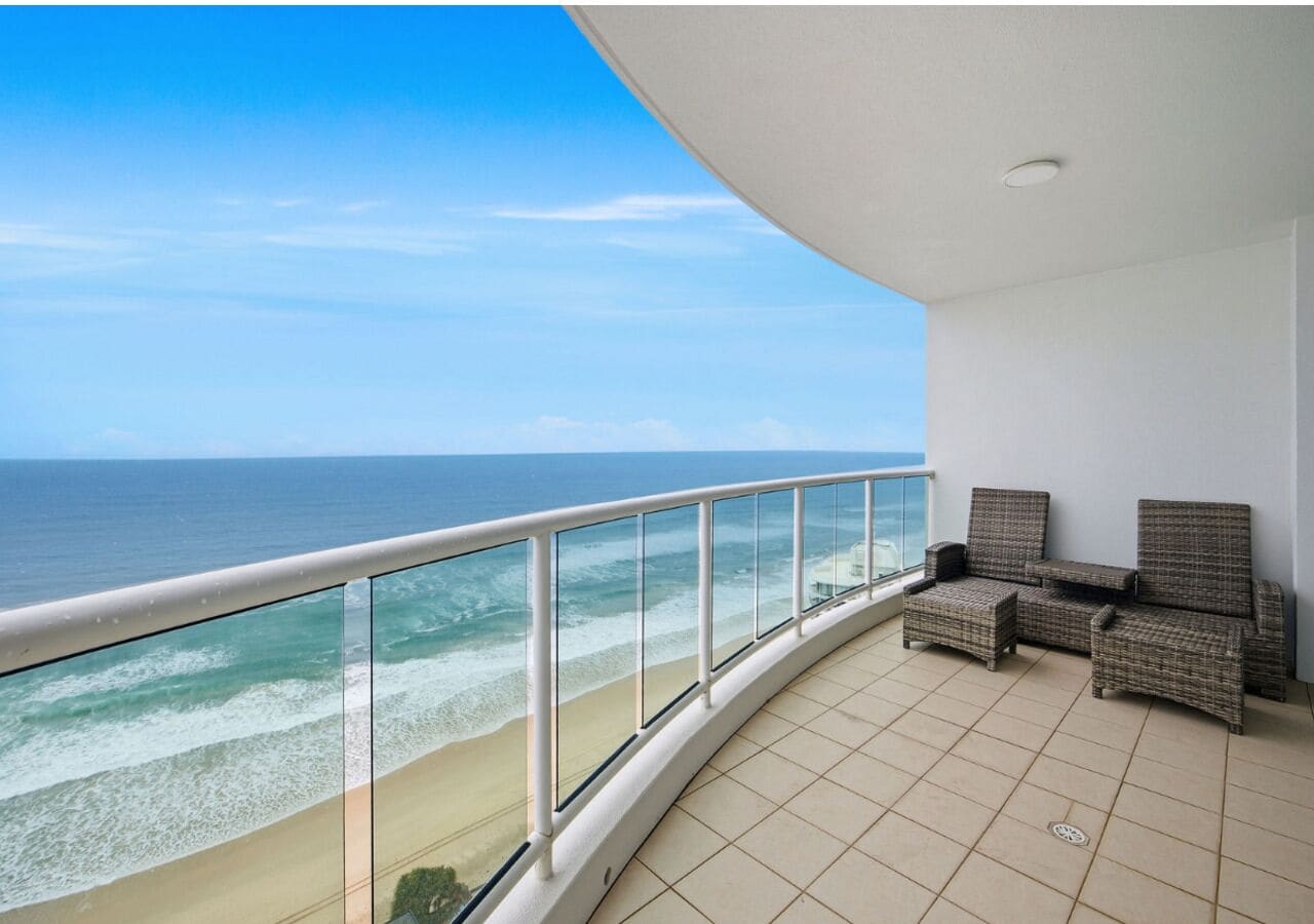 A balcony with a view of the ocean, a railing, and wicker furniture.