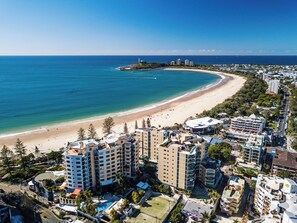 A coastal hotel with multiple buildings, a beach, and a lighthouse in the distance.