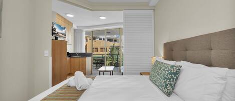 Ein Hotelzimmer mit Bett, einem kleinen Tisch, Blick auf einen Balkon und einer Küchenzeile.