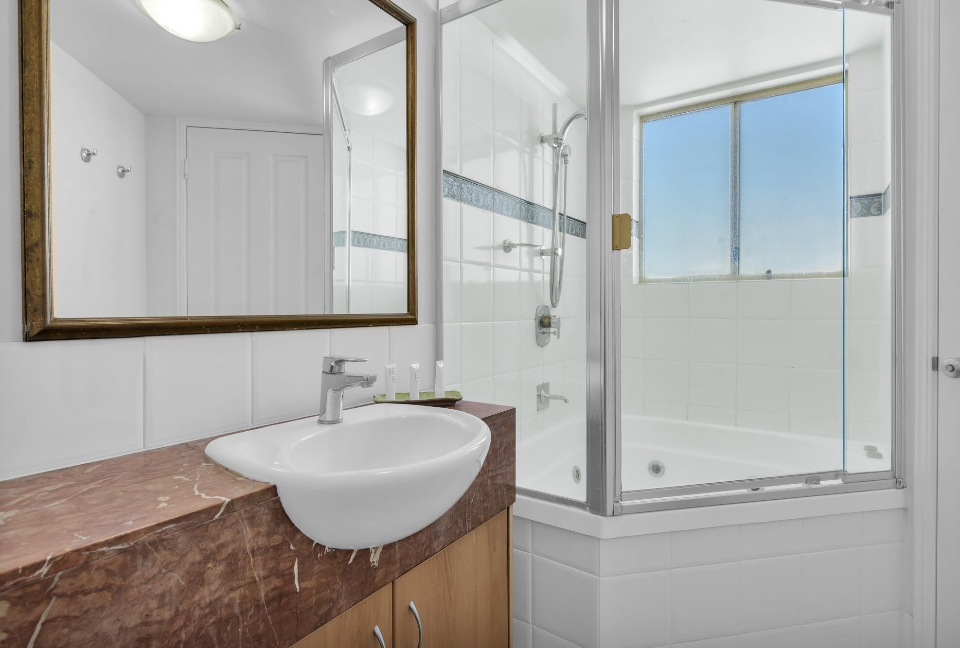 Un baño con lavamanos blanco, un espejo grande y una ducha con cerramiento de vidrio.