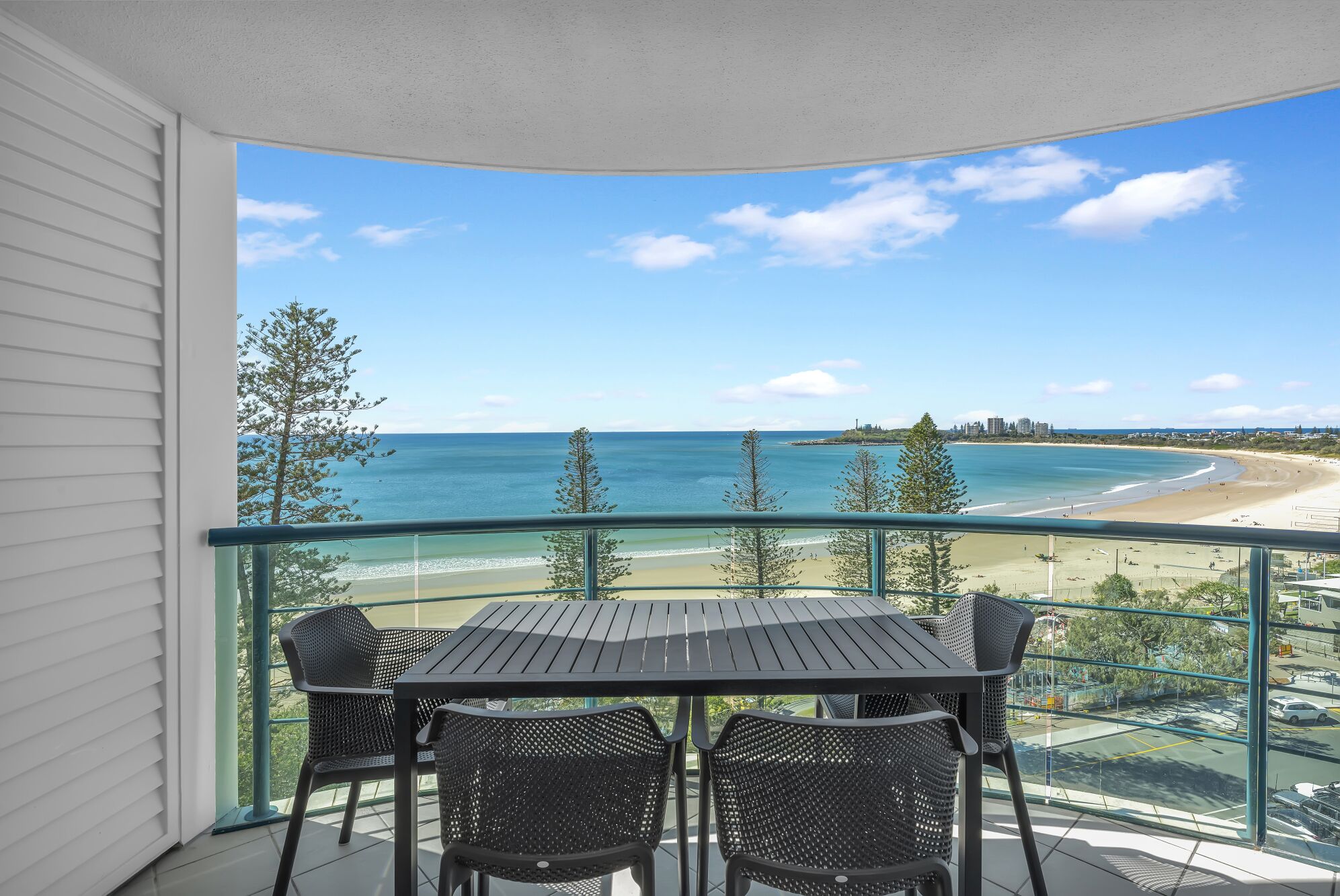 A balcony with a table and chairs, overlooking a beach and ocean.
