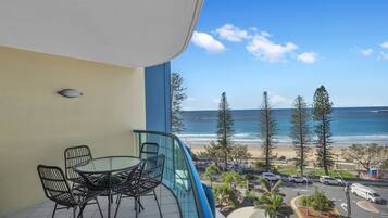 A balcony with a table and chairs, overlooking a beach and ocean.