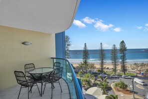A balcony with a table and chairs, overlooking a beach and ocean.