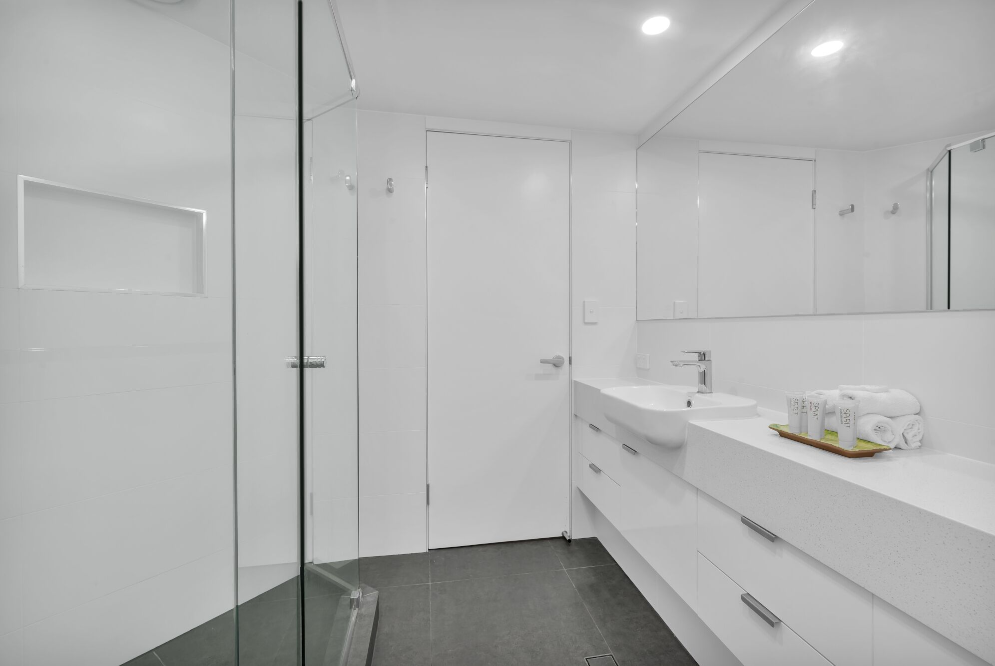 Casa de banho moderna com cabine de duche em vidro, lavatório branco e espelho.