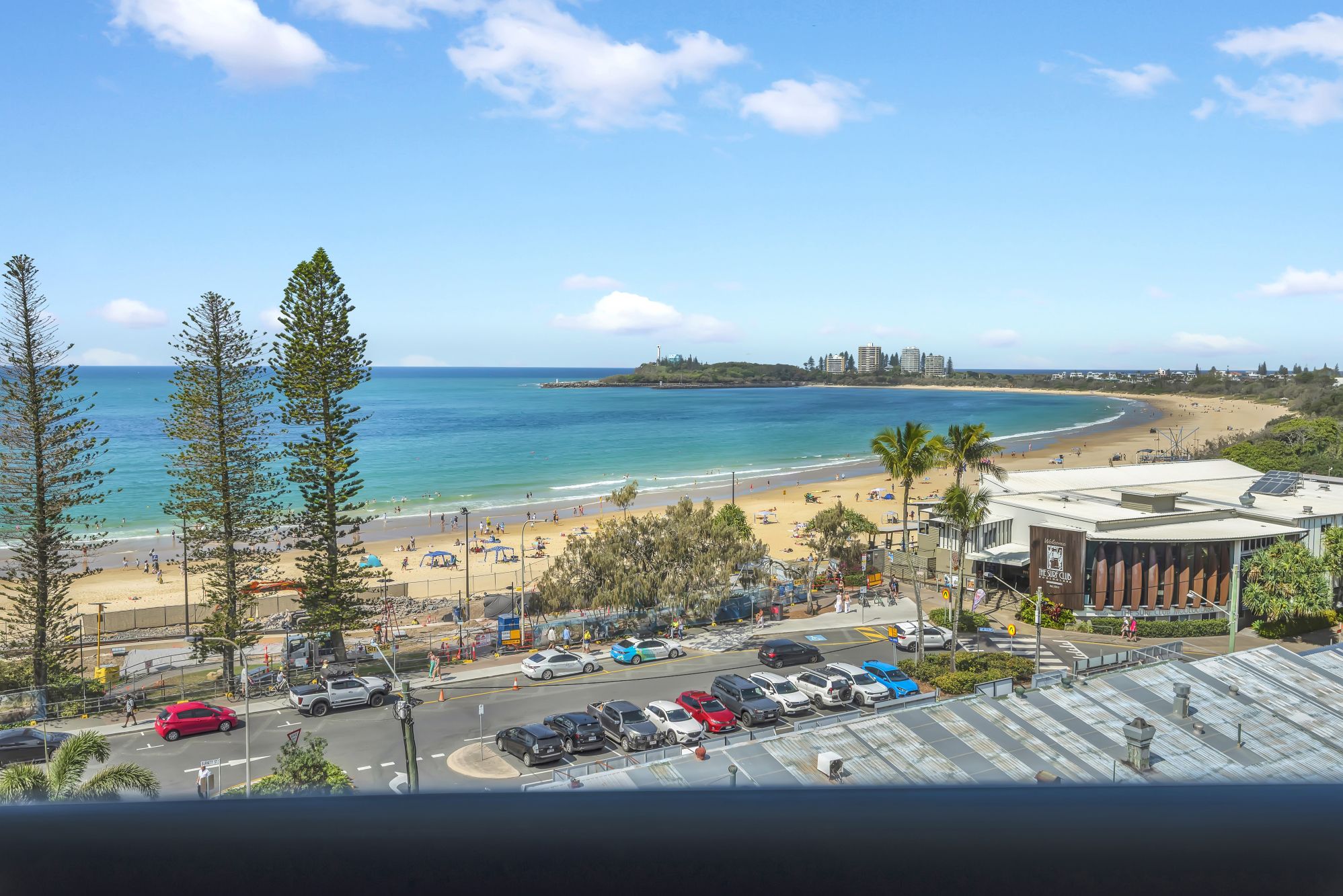 A coastal view with a beach, parking area, and a building with solar panels.