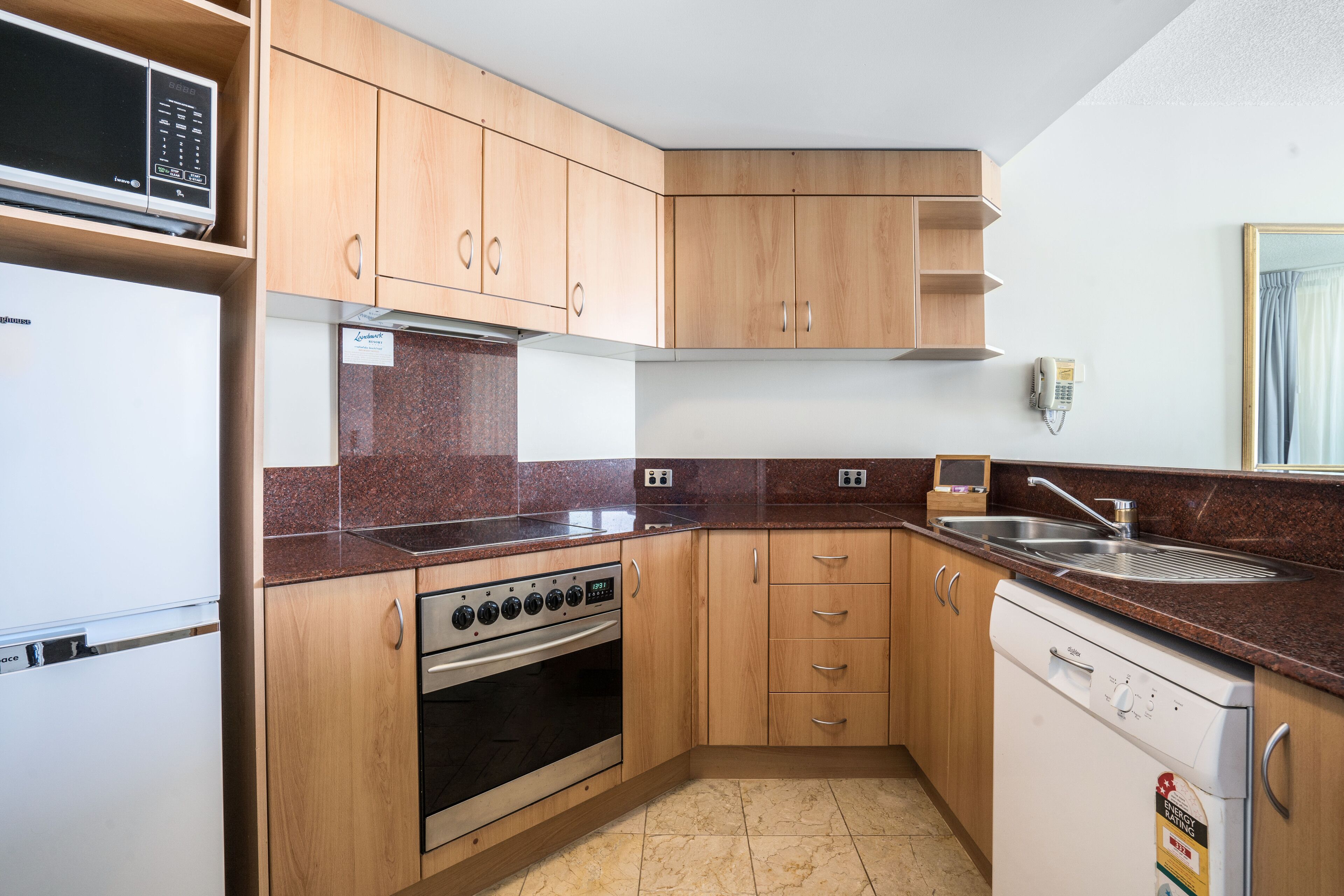A compact kitchen with wooden cabinets, a built-in microwave, a stove, and a dishwasher.