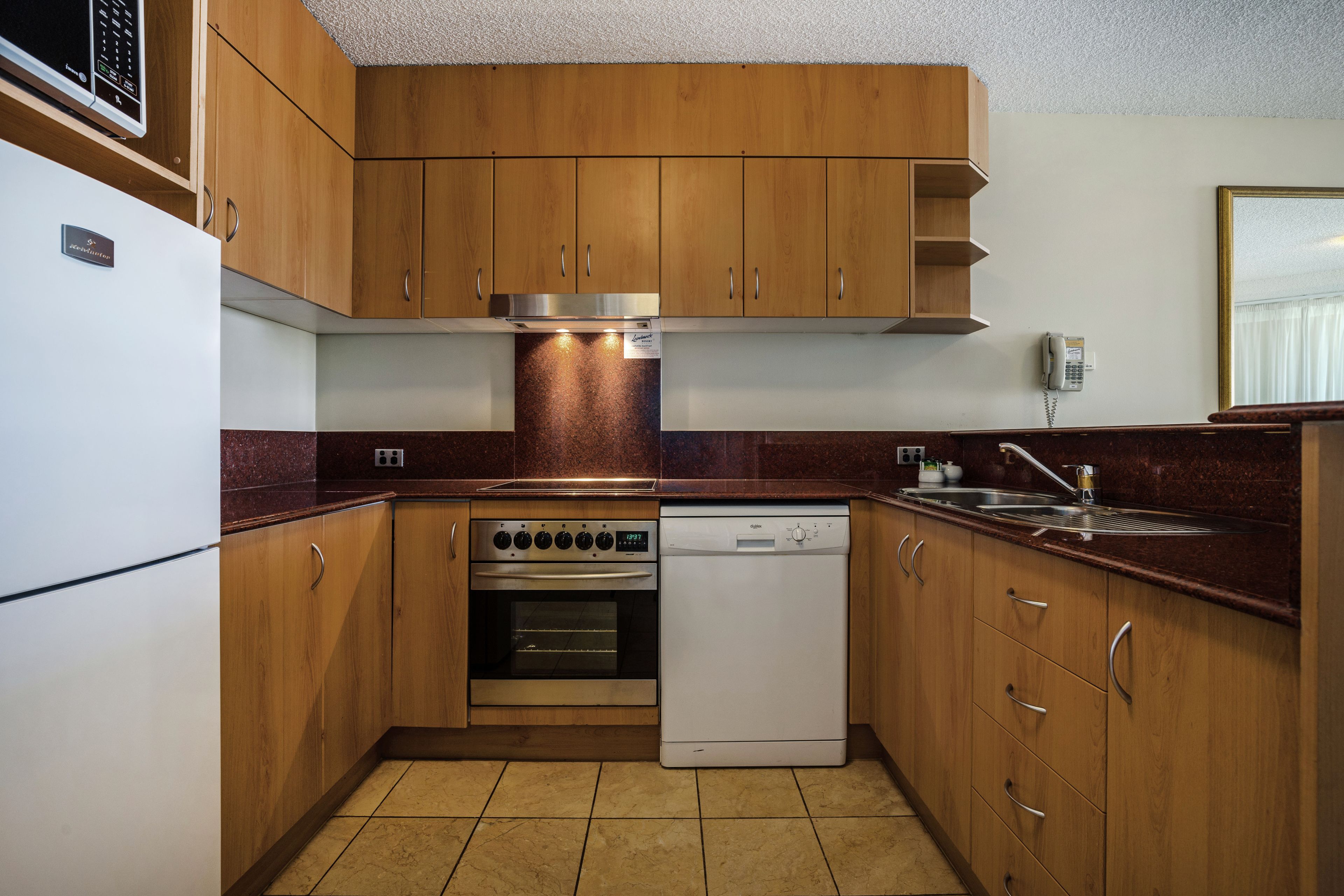 A compact kitchen with wooden cabinets, a built-in oven, a dishwasher, and a microwave.
