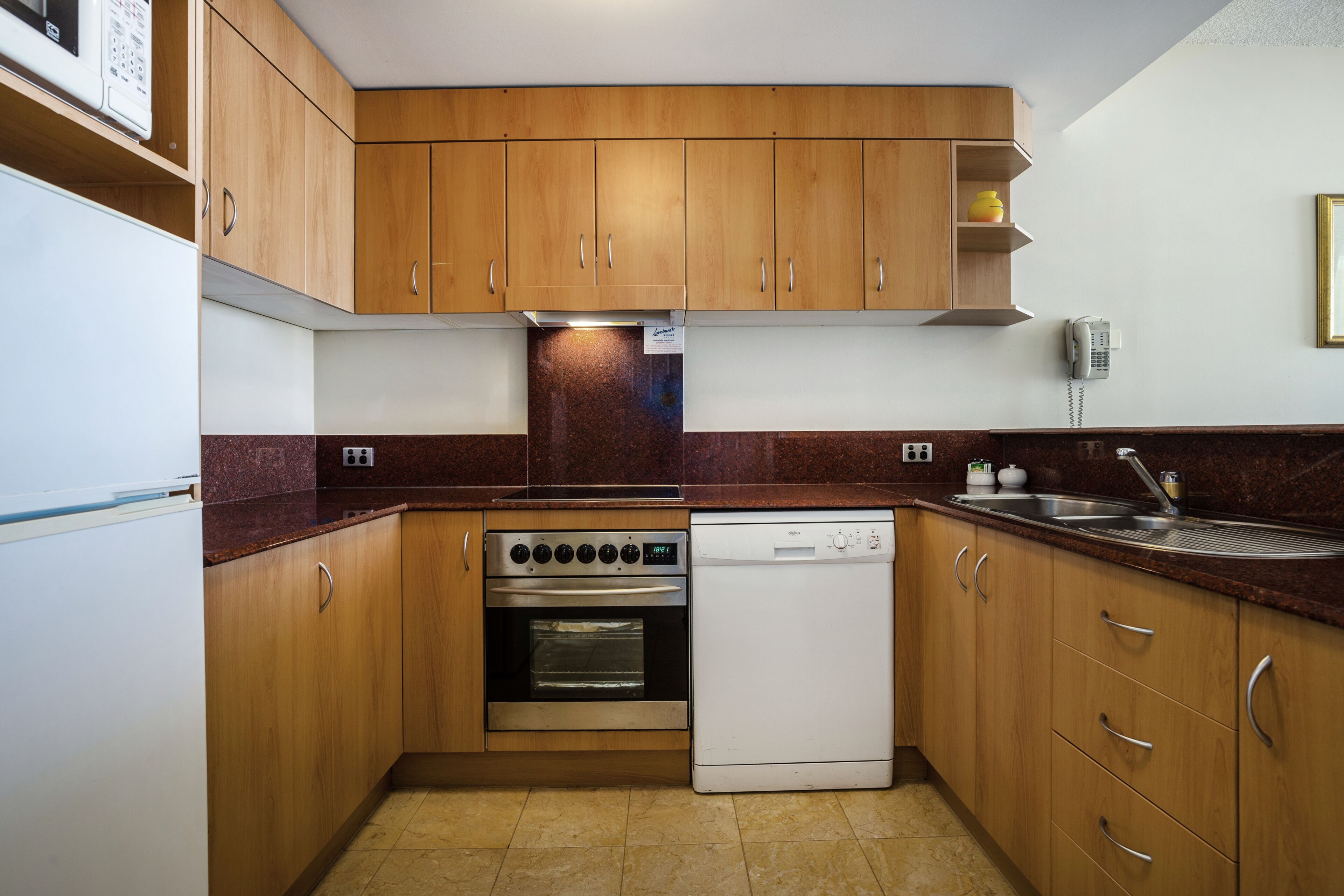 A compact kitchen with wooden cabinets, a built-in oven, a dishwasher, and a stainless steel sink.
