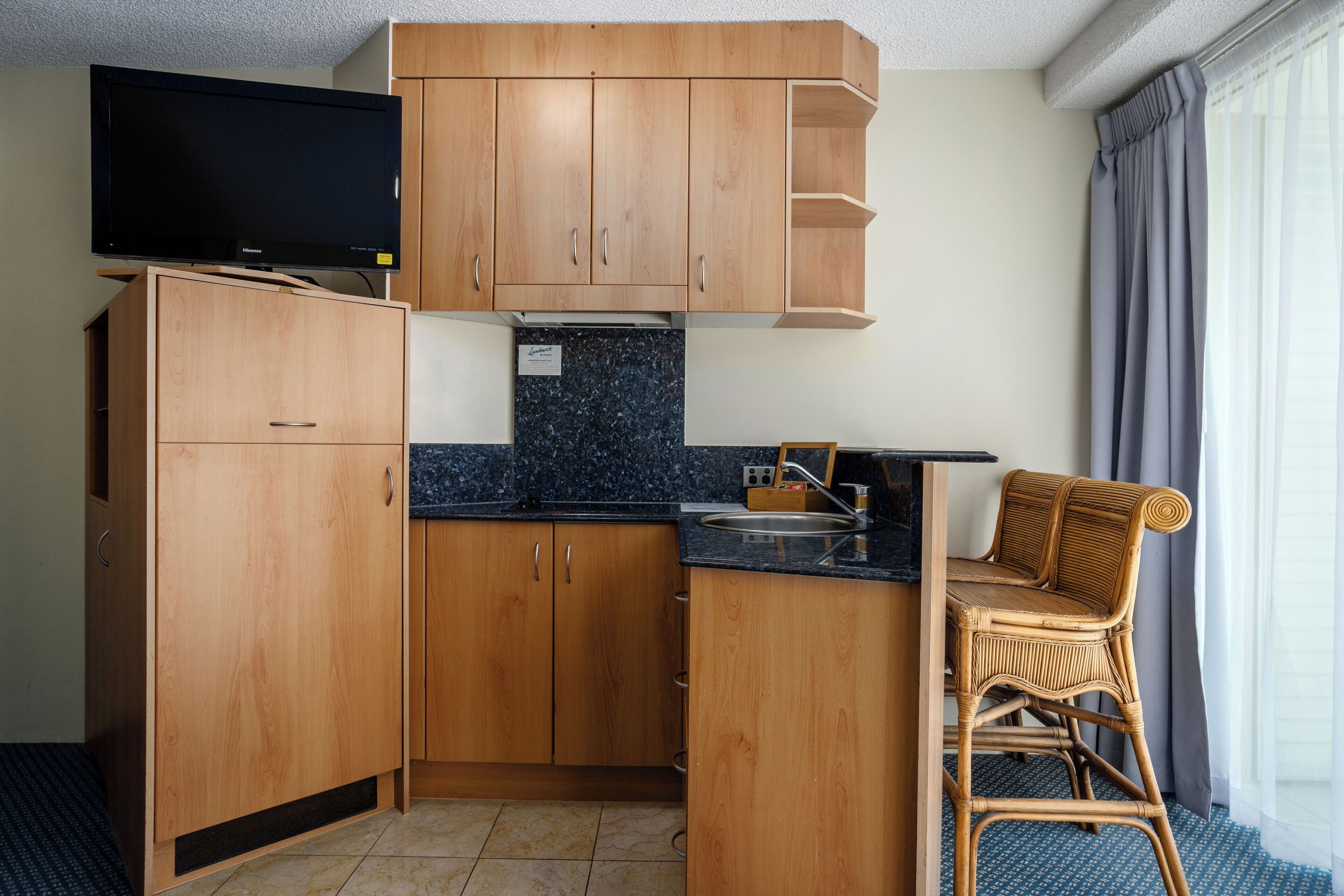Una cucina compatta con mobili in legno, una TV integrata e una sedia in vimini.