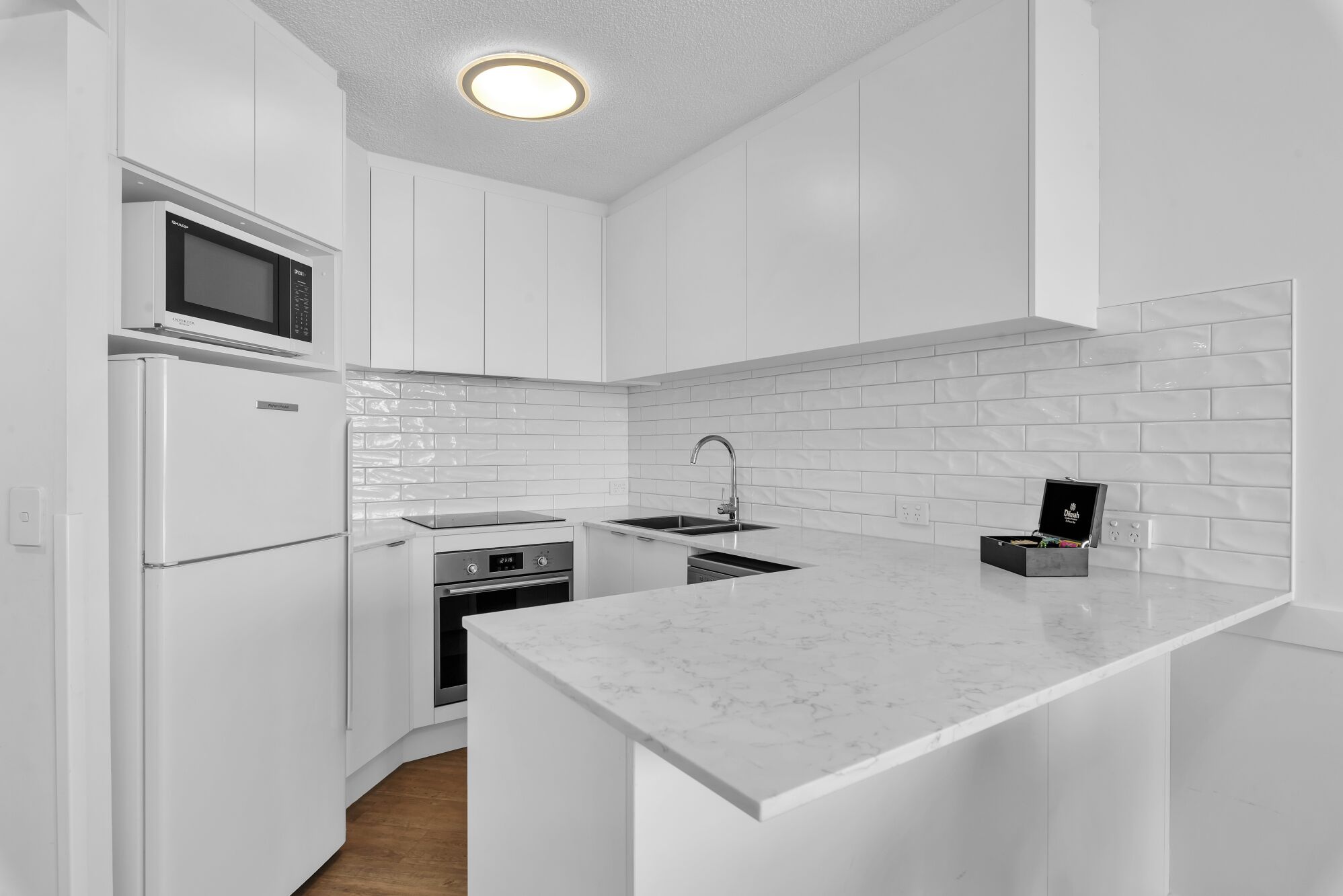 A modern kitchen with white cabinetry, a built-in oven, microwave, and a sink with a black countertop.