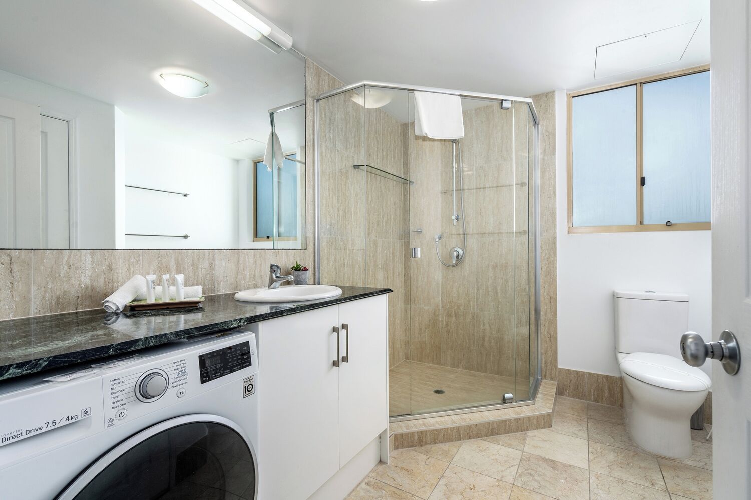 Een moderne badkamer met een glazen douchecabine, een wastafel met toiletartikelen en een wasmachine.