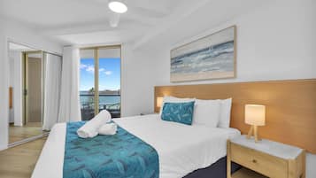 A hotel room with a bed, a nightstand, a painting, and a view of the sea.