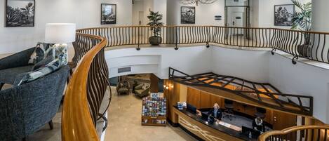 A spacious lobby with a wooden staircase, a reception desk, and a seating area with a sofa and armchairs.