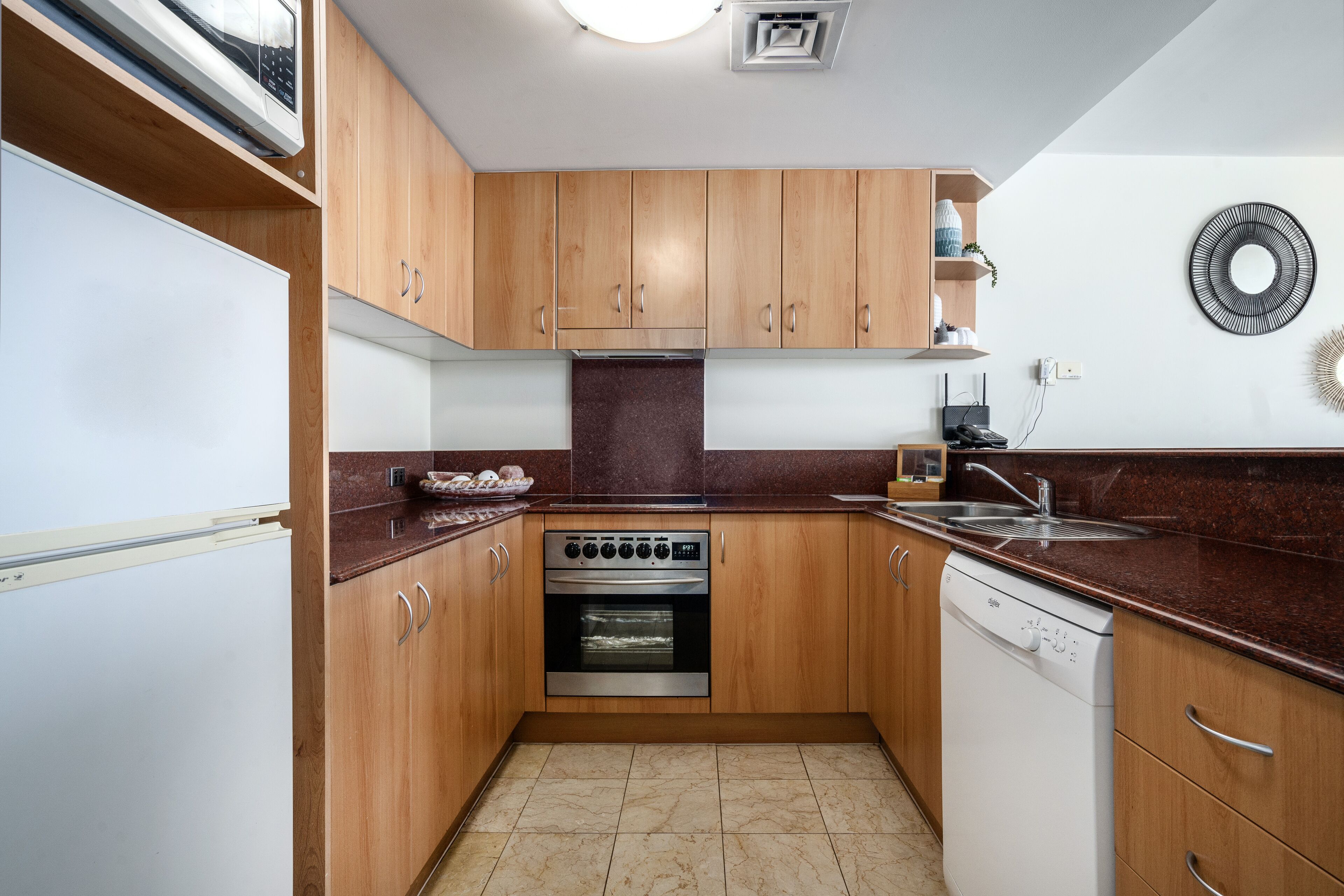 A compact kitchen with wooden cabinets, a built-in oven, a dishwasher, and a stainless steel sink.