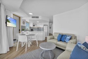 A modern living room with a sofa, a coffee table, and a dining area with chairs and a small table. - Landmark Resort (Mooloolaba)