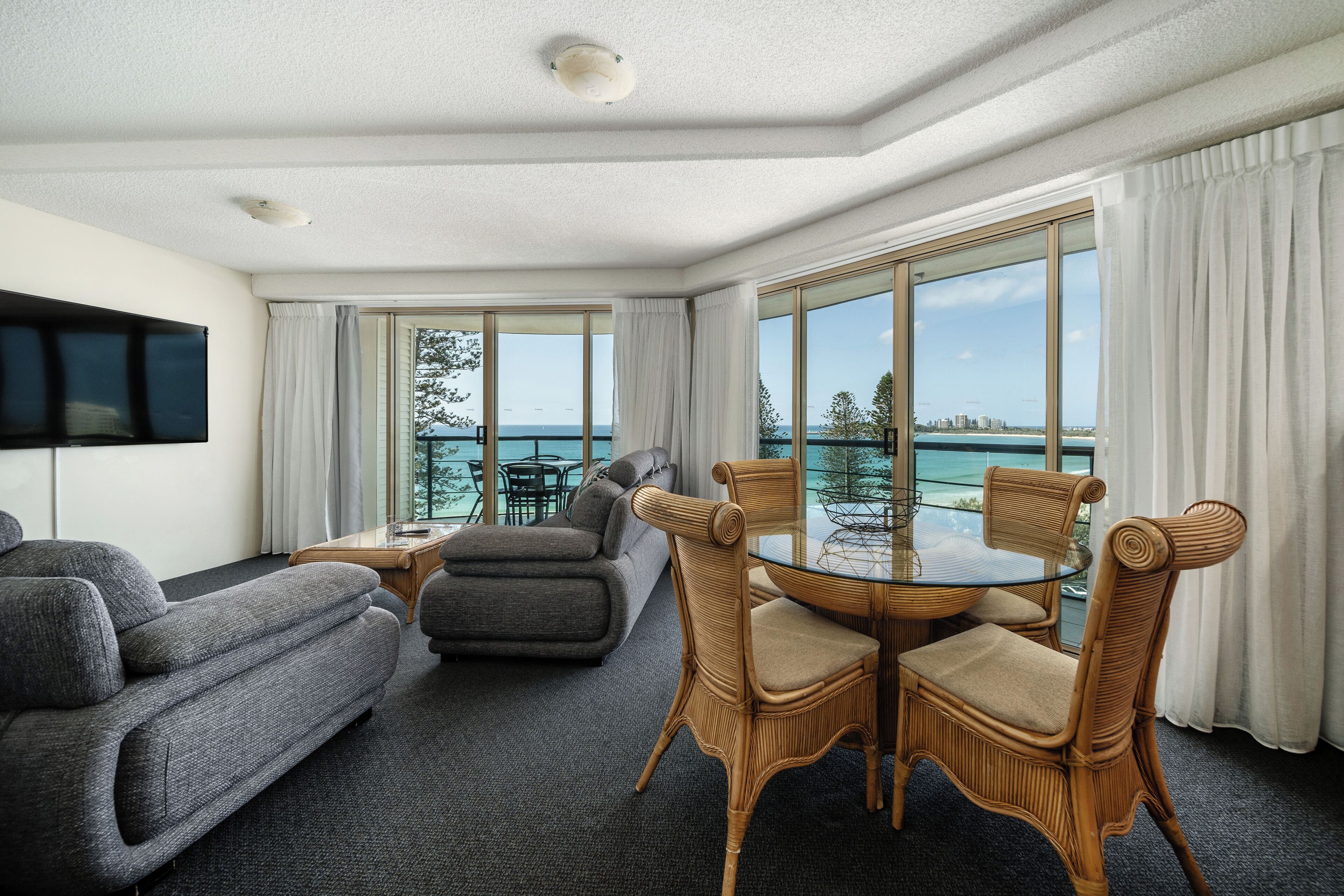 Un hotel moderno con amplias ventanas que ofrecen vistas al mar, un sofá confortable, una mesa de comedor con sillas y un televisor de pantalla plana montado en la pared.