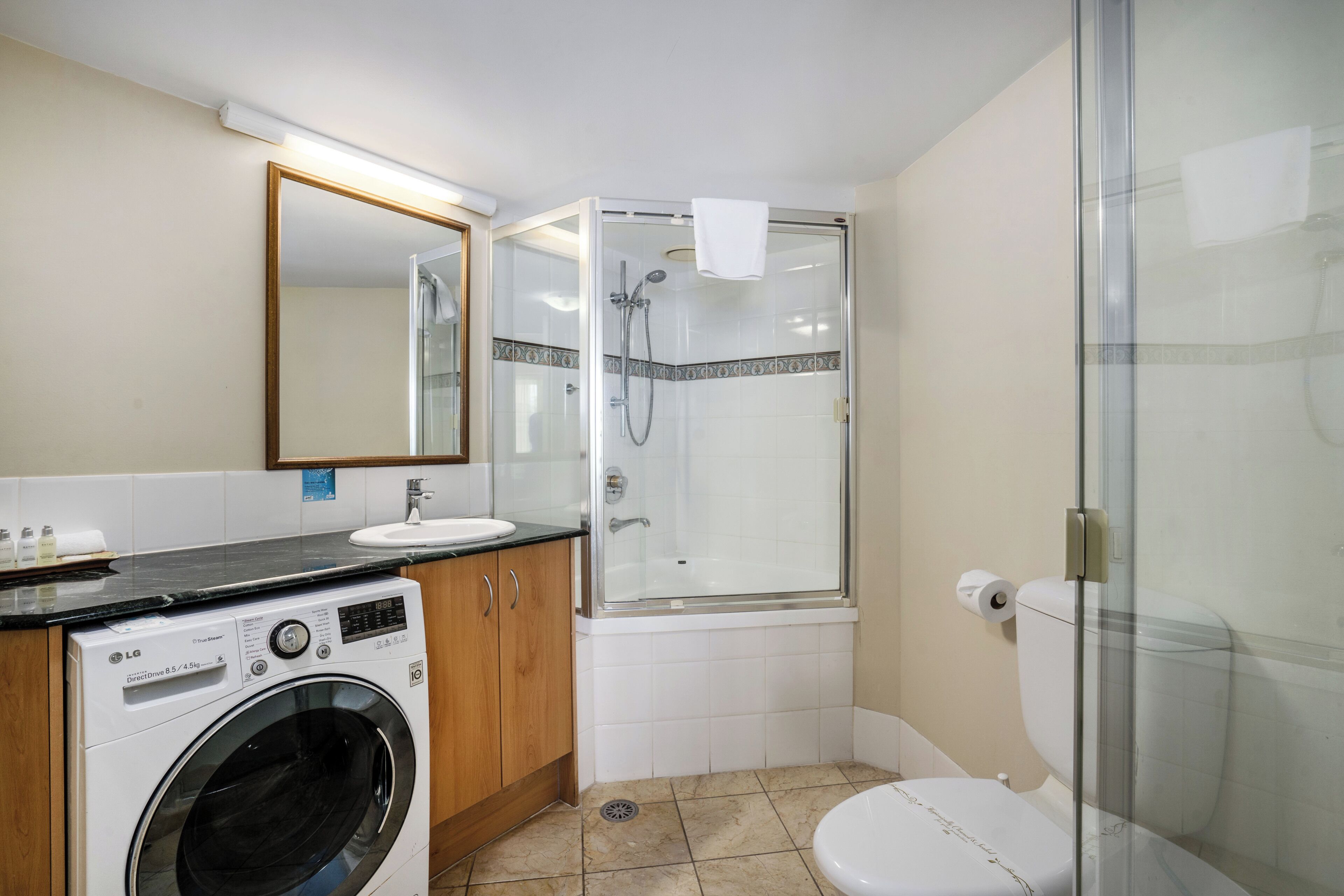 A bathroom with a washing machine, sink, toilet, and glass-enclosed shower.