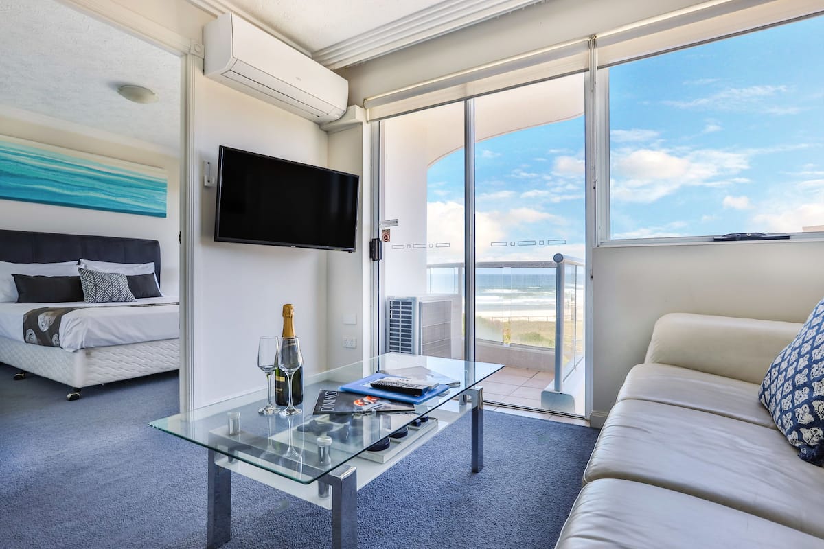 A modern hotel room with a bed, a glass coffee table, a TV, and a balcony with a view.
