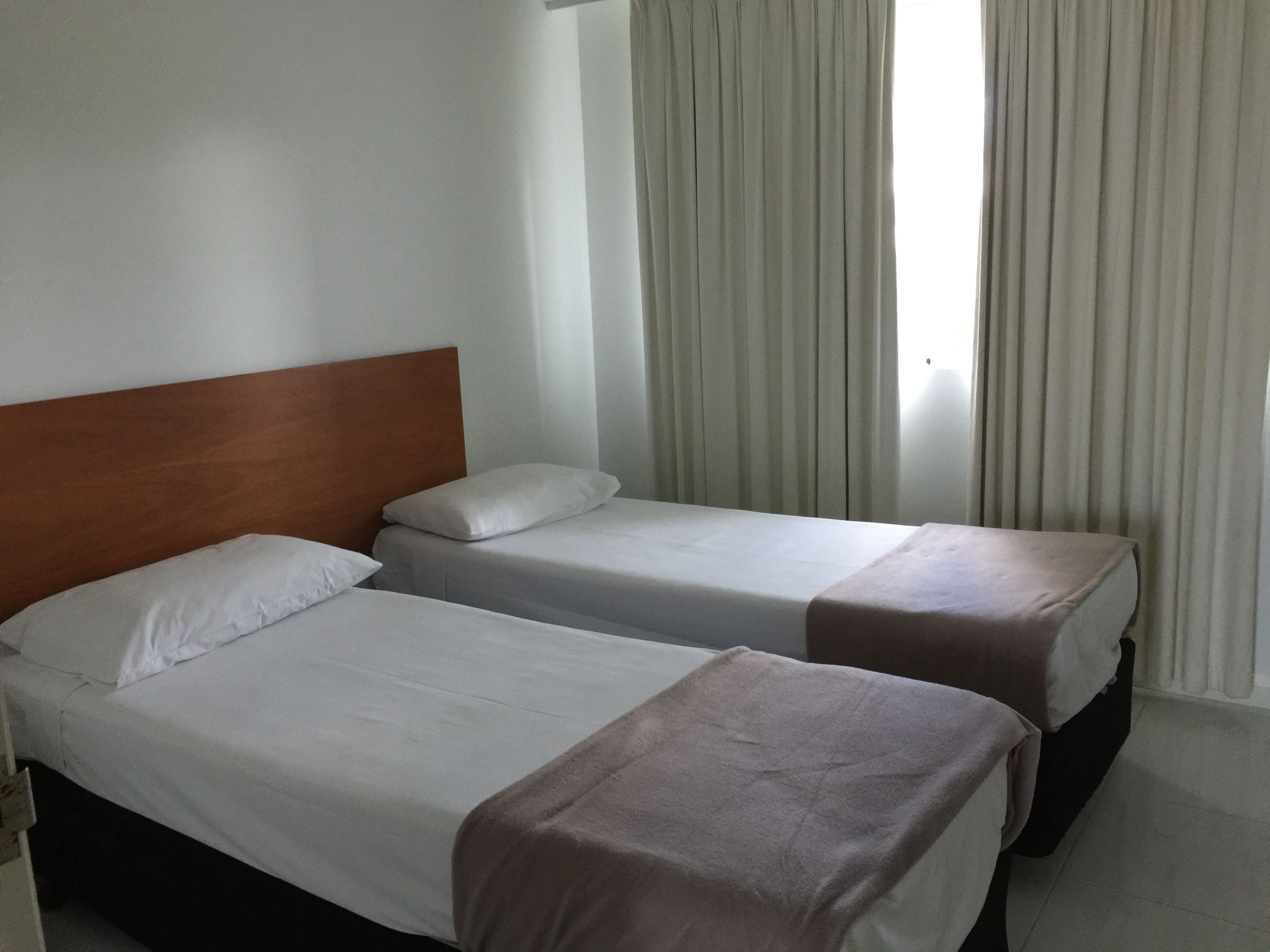 A hotel room with two beds, a wooden headboard, white bedding, and a window with curtains.