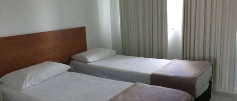 A hotel room with two beds, a wooden headboard, white bedding, and a window with curtains.