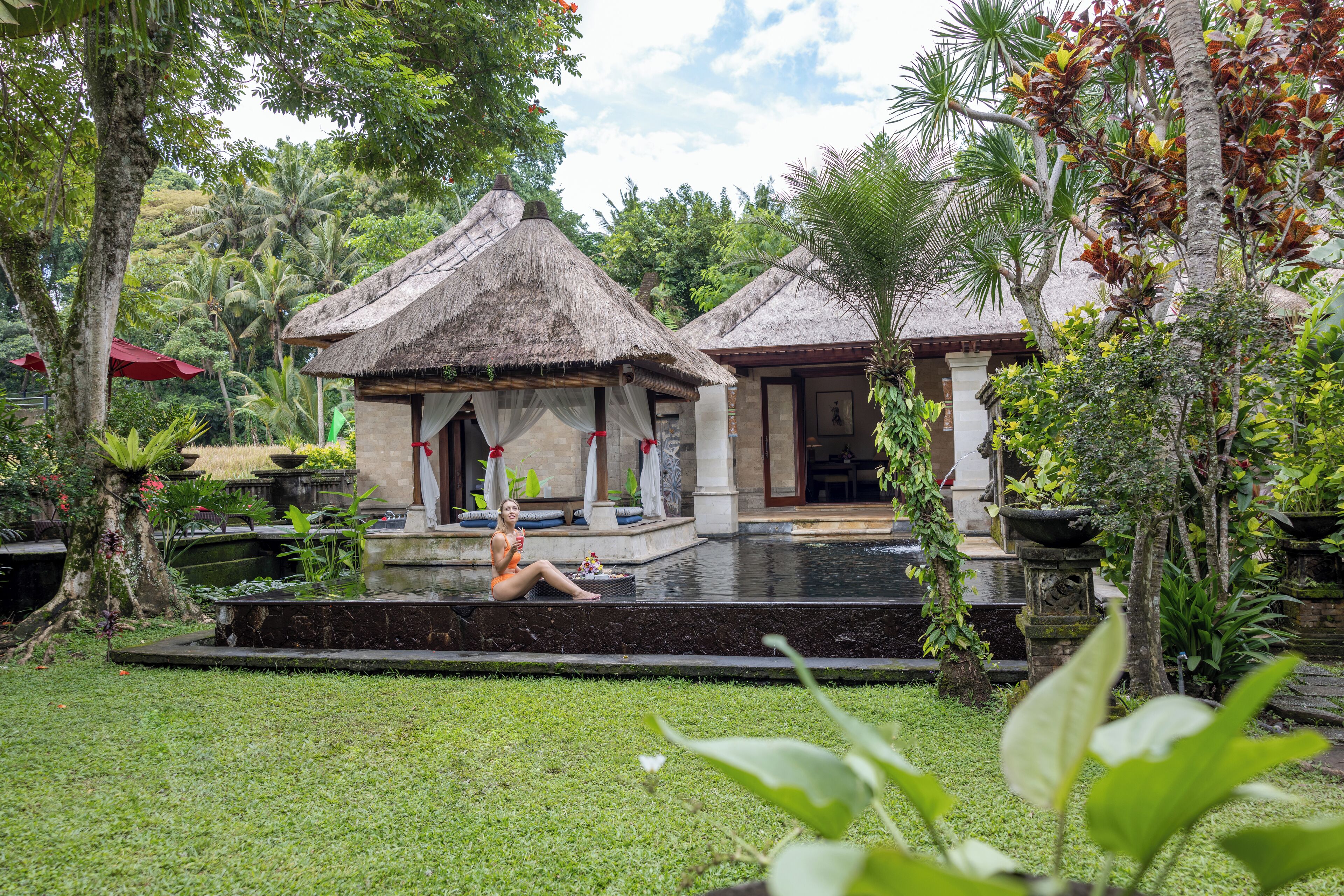 A tropical resort with thatched-roof structures, a swimming pool, and lush greenery.