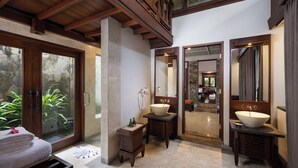 A bathroom with a large stone-tiled floor, wooden vanity with a large basin, and a glass door leading to a balcony with plants. - Arma Museum & Resort (Ubud)