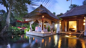 A serene pool area with a thatched-roof gazebo, a well-lit indoor space, and lush tropical surroundings. - Arma Museum & Resort (Ubud)