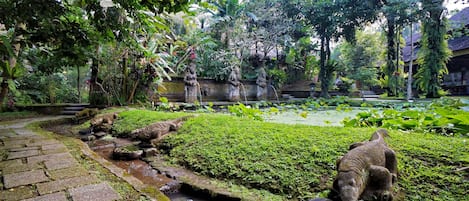 Un jardin avec des allées pavées de pierres, un étang et une statue.