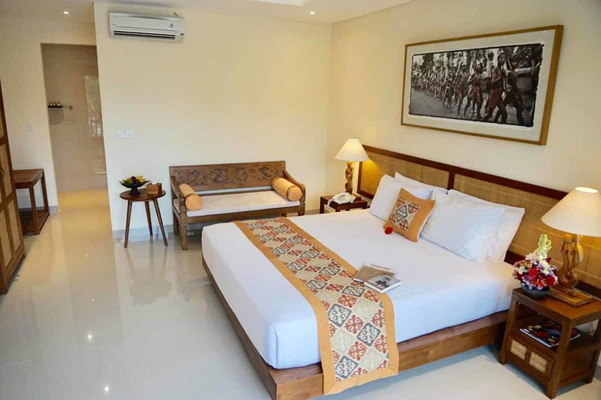 Habitación de hotel con una cama grande, un sofá más pequeño, una mesita de noche con lámpara y un aire acondicionado instalado en la pared.