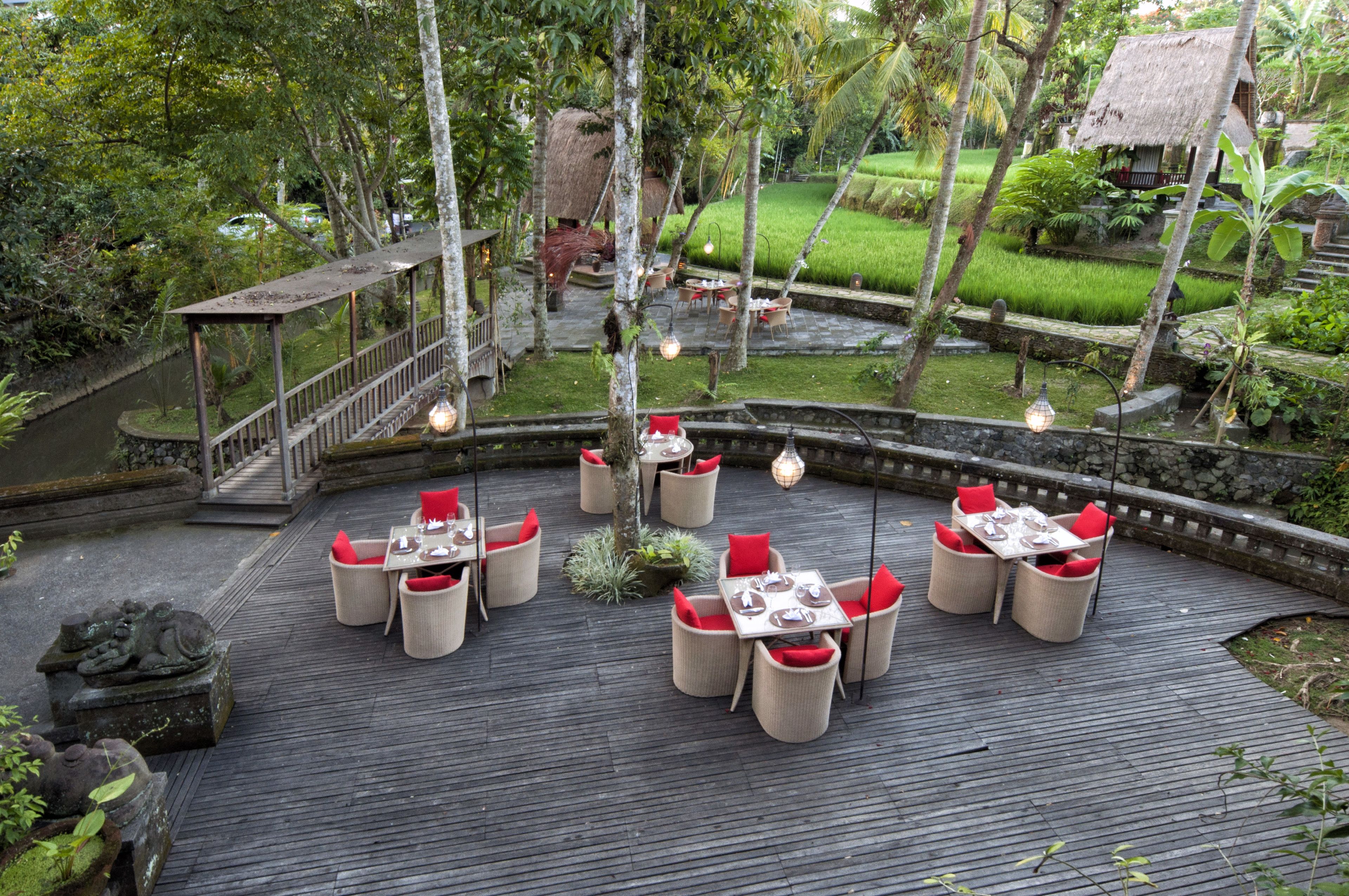 An outdoor dining area with tables and chairs, surrounded by greenery and a water feature.